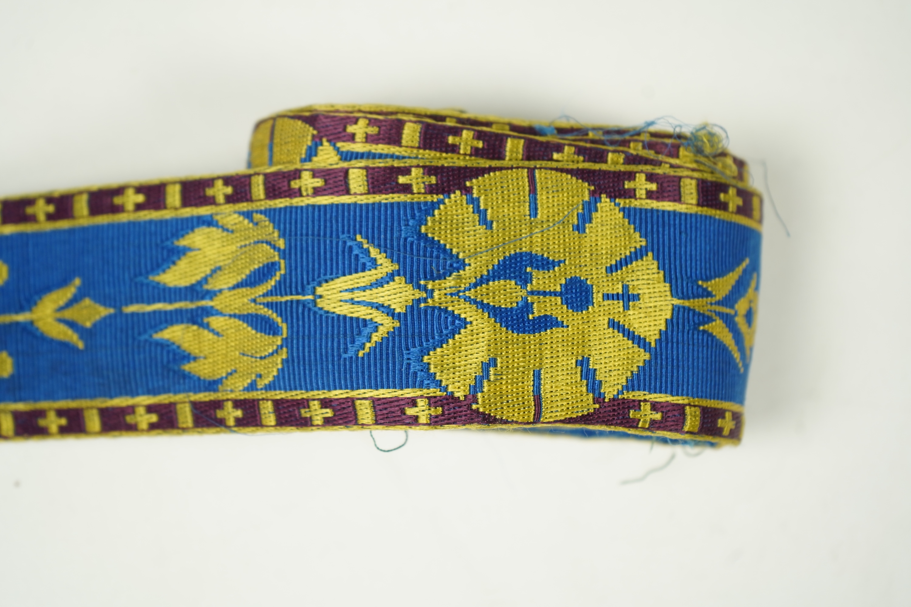 Three long lengths of late 19th century silk woven braiding. One woven in gold, turquoise and maroon silk, possibly for ecclesiastic use, in Christopher Dresser ‘style’ motifs, another in gold and black silk thread in a